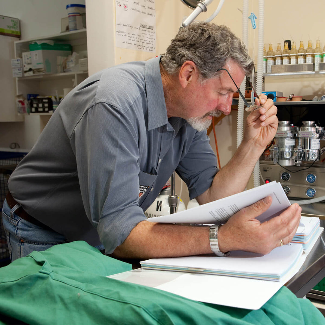 Man inspecting green organic fermented dog supplement package with lab equipment in background.
